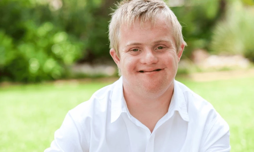 Boy with down syndrome sitting in park and smiling at camera